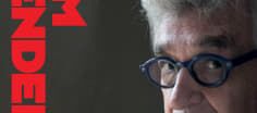 Foto eines Portraits von Wim Wenders, das auf der rechten Hälfte des Bildes ist. Der Hintergrund ist schwarz. Auf der linken Seite des Bildes steht sein Name senkrecht in roten Großbuchstaben.