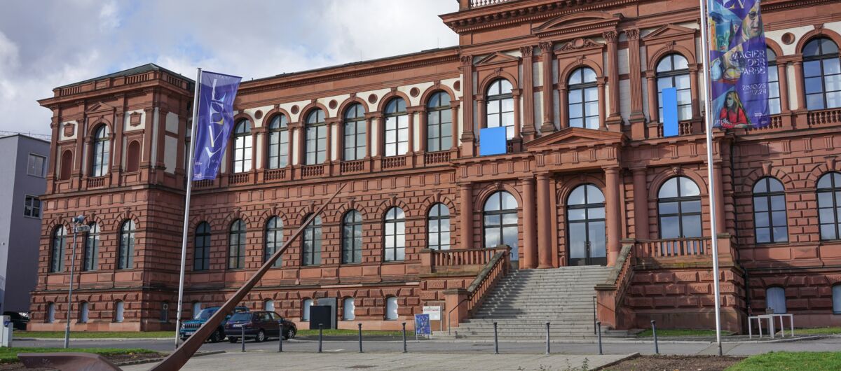 Außenansicht des Museums aus 1874, dessen Fassade aus braunem Stein mit Rundbögen und vielen Fenstern besteht. Eine breite Treppe führt zum von Säulen gezierten Eingang. Auf dem flachen Dach gibt es eine Empore mit kleinem Aufbau.