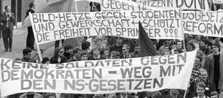 Schwarz-weiß Foto eines Demonstrationszugs am 11.05.1968 gegen die Notstandsgesetze. Größtenteils jüngere Menschen sind zu sehen. Sie halten weiße Transparente - beschrieben mit ihren Forderungen - hoch.