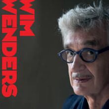 Foto eines Portraits von Wim Wenders, das auf der rechten Hälfte des Bildes ist. Der Hintergrund ist schwarz. Auf der linken Seite des Bildes steht sein Name senkrecht in roten Großbuchstaben.