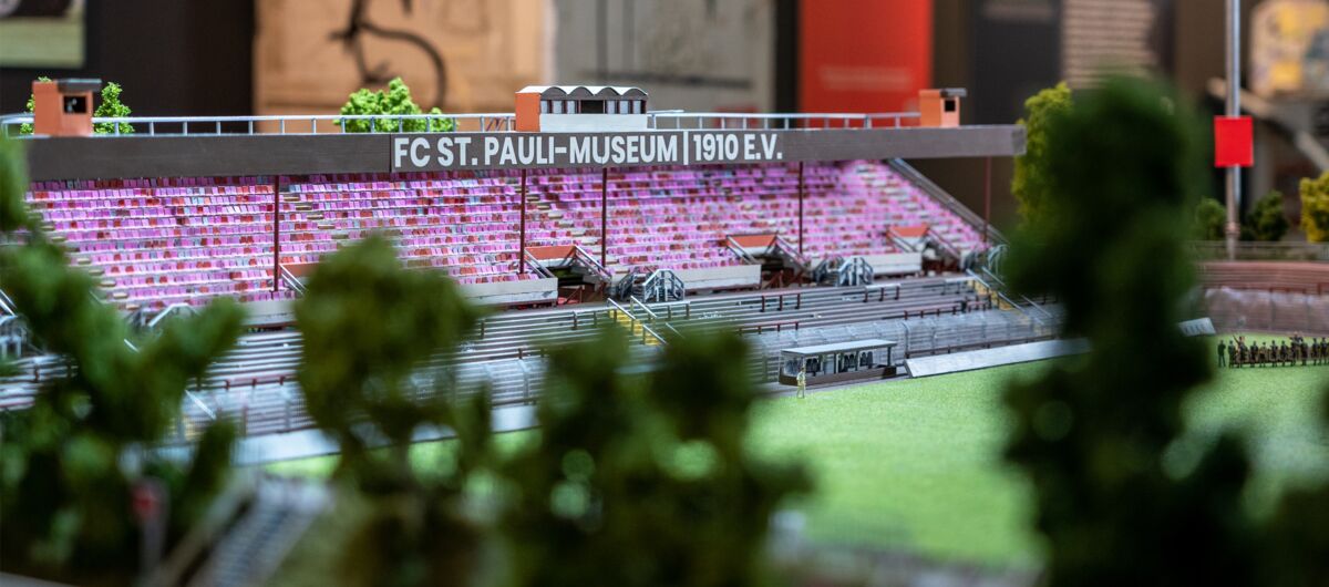 Modell des FC St. Pauli Stadions mit Teilen der Tribüne, des Rasens und Fans auf den Rängen.