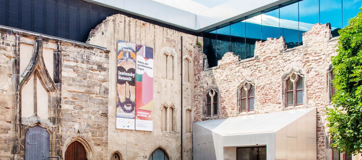Foto der Außenansicht des Kunstmuseum Moritzburg Halle (Saale). Die eigentliche historische Fassade ist aus Stein und durch alten Türen und Fenstern unterbrochen. Hinter dieser ist eine moderne verglaste Fassade darüber zu sehen.