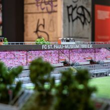 Modell des FC St. Pauli Stadions mit Teilen der Tribüne, des Rasens und Fans auf den Rängen.