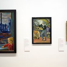 Foto einer weißen Ausstellungswand an der drei gerahmte Gemälde hängen. Von links nach rechts werden diese kleiner. Auf ihnen werden Alltagssituationen dargestellt, in denen Menschen im Mittelpunkt stehen.