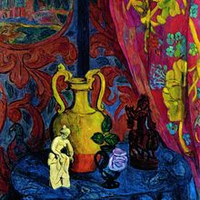Gemälde, auf dem ein Stillleben abgebildet ist. Auf einem runden kleinen Tisch mit blauer Tischdecke stehen eine gelbe Vase, zwei Figuren und eine kleine Vase mit blauer Rose. Der Hintergrund wird durch bunte Wände und Stoffe definiert.