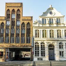 Foto einer historischen Häuserreihe. Auf der rechten Seite des Fotos ist mit weißer Fassade das dreistöckige Buddenbrookhaus zu sehen. Die linke Seite wird durch einen ähnlich hohen Klinkerbau mit großem Durchgang zum Hinterhof dominiert.
