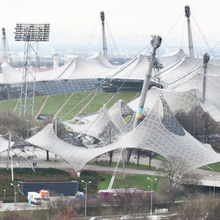 Foto der Zeltdachkonstruktion des Münchener Olympiastadions. Wie Spinnennetze sind die weiß durchsichtigen Dächer über die relevanten Areale gespannt.