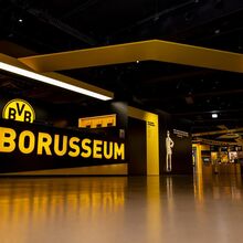 Vom Boden aufgenommenes Foto. Links eine Theke, auf der "Borusseum" steht. Dahinter das BVB-Logo. Rechts gehen die Ausstellungsräume ab. Die Vereinsfarben werden durch schwarze Wände und gelbe Buchstaben, Logos und Ausstellungsinhalte wiedergespiegelt.