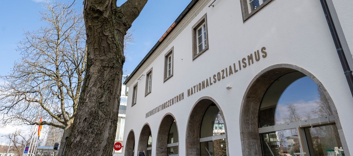 Foto der Außenansicht des Dokumentationszentrums Nationalsozialismus der Museen Freiburg. Fünf Rundbögen mit Fensterglas prägen die Hausfront im Erdgeschoss. Darüber ist der Schriftzug Dokumentationszentrum Nationalsozialismus zu lesen.