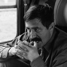 Schwarz-weiß Foto von Günter Grass in einem Zugabteil. Er sitzt am Fenster und schaut auf den gegenüberliegenden Sitz. Sein rechtes Bein ist aufgestellt, die Ellenbogen auf die Knie gestützt, die Hände gefaltet und die Daumenspitzen an die Zähne gelegt.