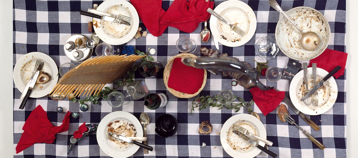 Foto von oben auf einen Esstisch nach dem Essen. Auf einem blau-weiß karierten Tischtuch stehen sechs schmutzige Teller mit Besteck, Servietten, Gläsern, Flaschen, Suppenteriene, Brotkorb, Gewürzen und wenig Deko aus Blättern.